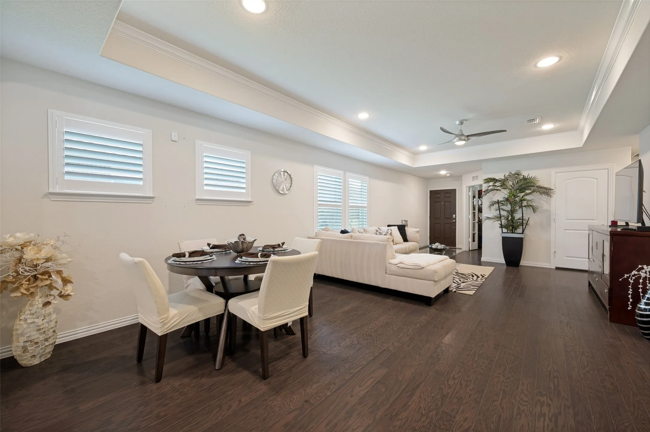 Tray ceiling with recessed lighting, dark wood-finish flooring, white plantation shutters, and a ceiling fan