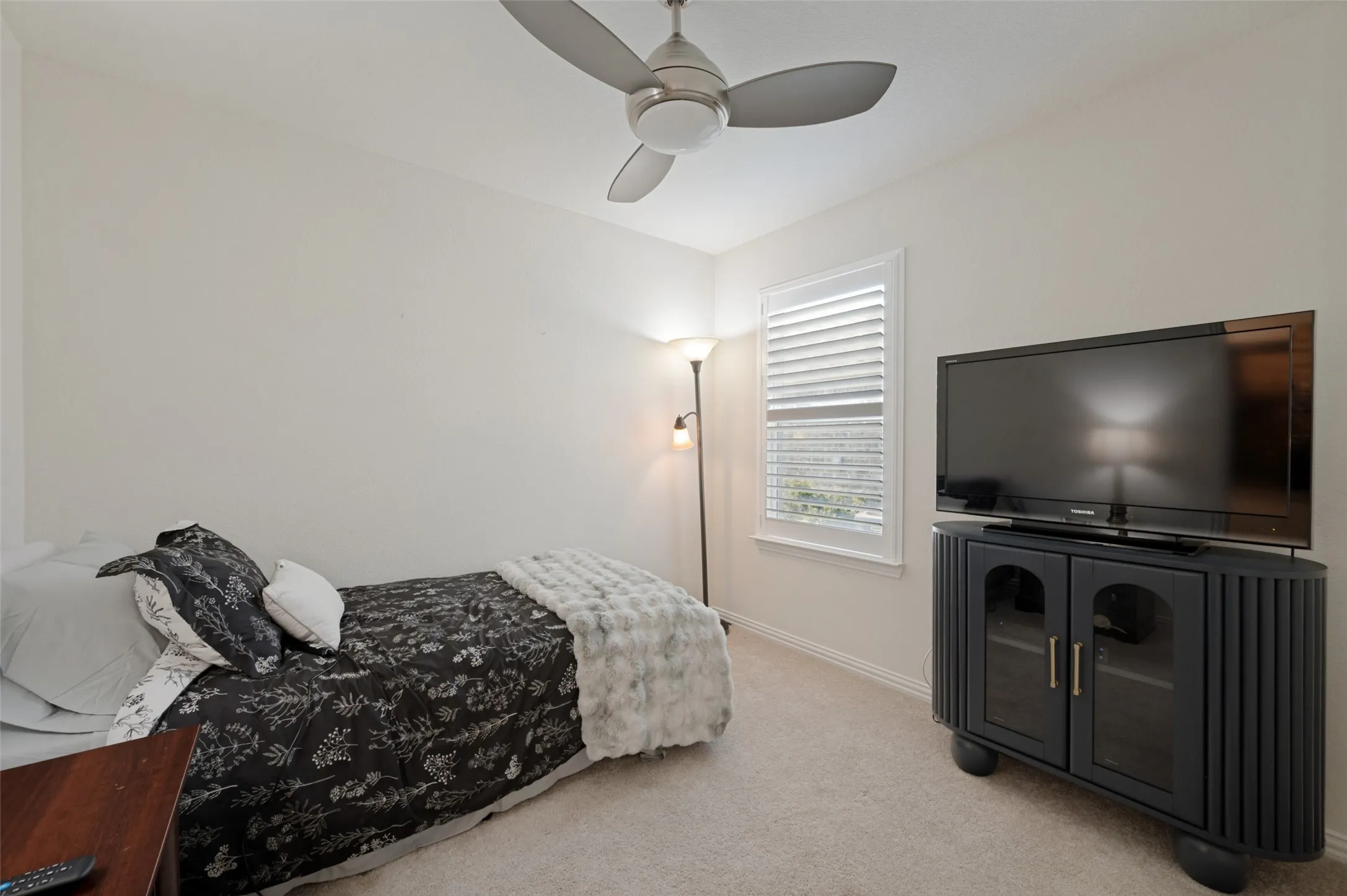 Neutral wall paint, carpet flooring, window with shutters, ceiling fan, and built-in media console