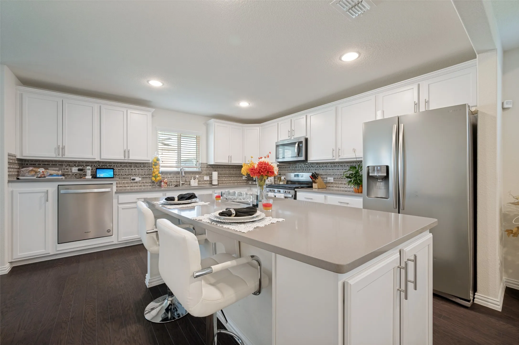 White shaker cabinetry, stainless steel appliances, dark wood-finish flooring, recessed lighting, and a kitchen island with seating