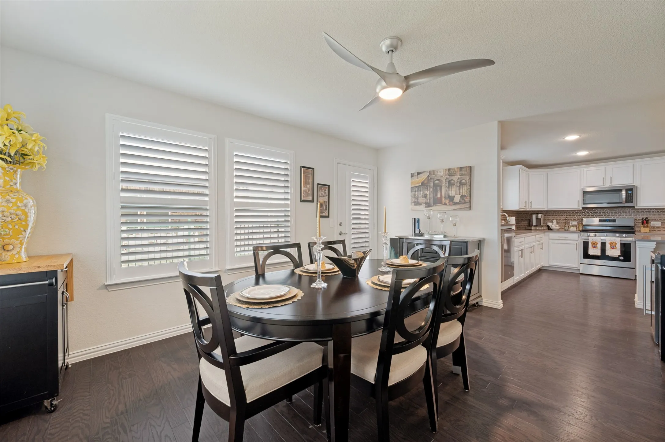 Open-concept dining area with dark wood-finish flooring, white walls, and a modern ceiling fan with integrated lighting