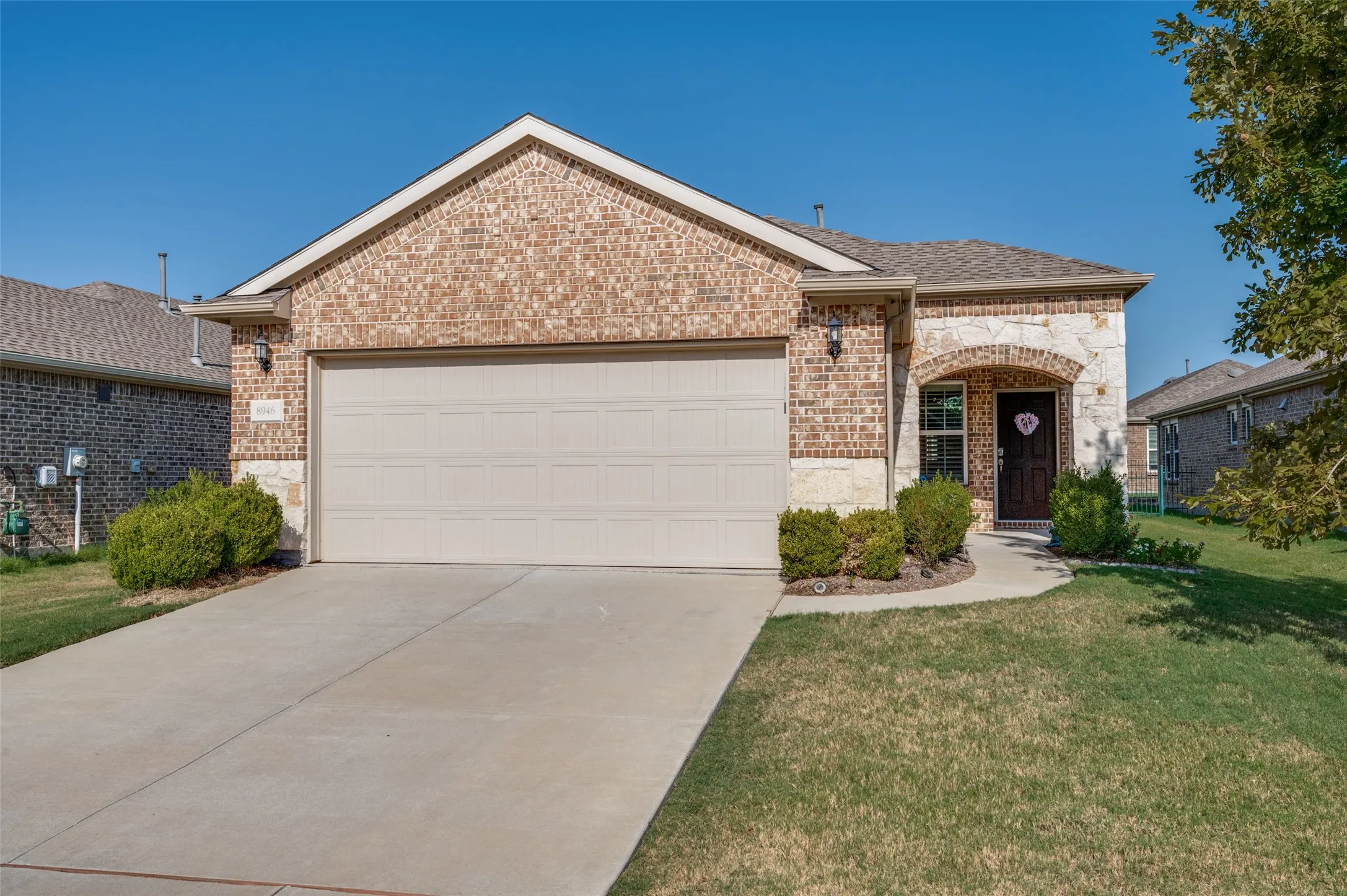 Brick and stone exterior with an arched entryway, attached garage, concrete driveway, and landscaped front yard
