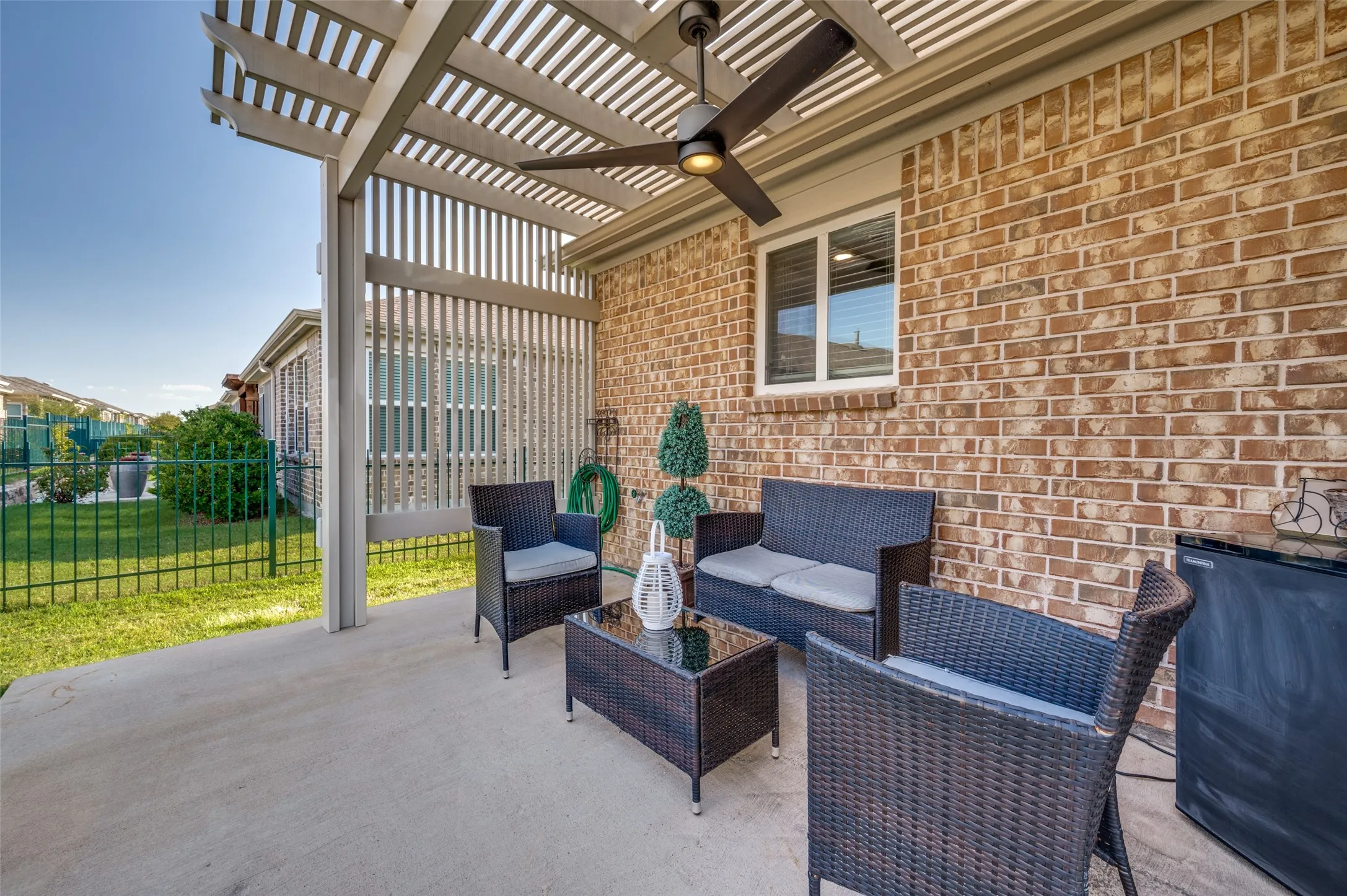 Covered concrete patio with a slatted pergola, ceiling fan, and brick exterior