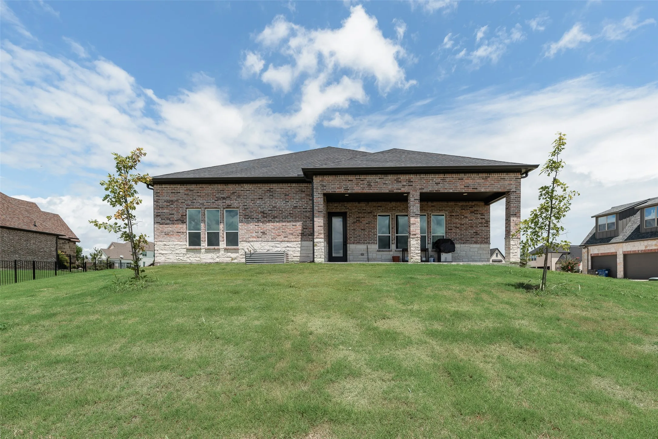 Expansive green lawn with a covered patio, brick and stone exterior, dark roof, and multiple windows