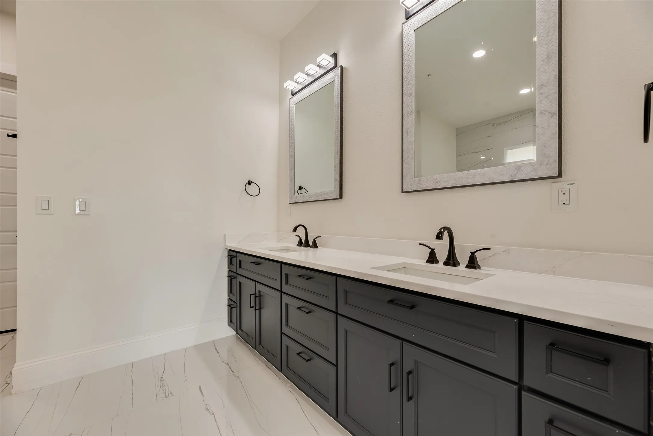 Dual vanity with dark cabinetry, integrated sinks, white countertops, and matte black fixtures