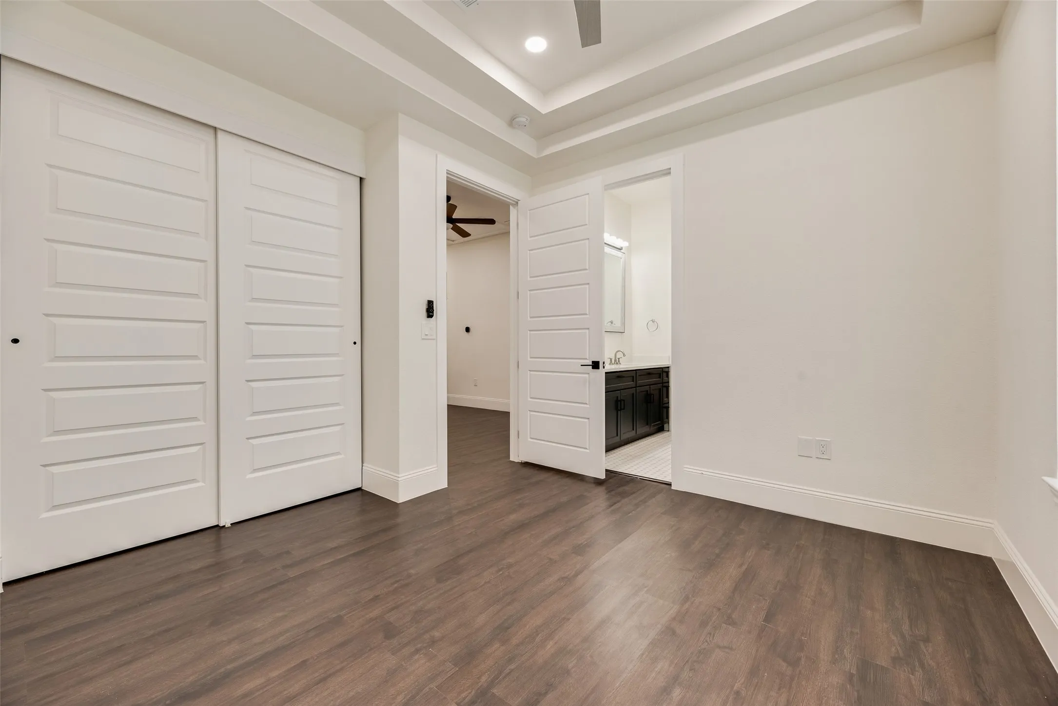 Wood-finish flooring, white paneled doors, tray ceiling, and a ceiling fan