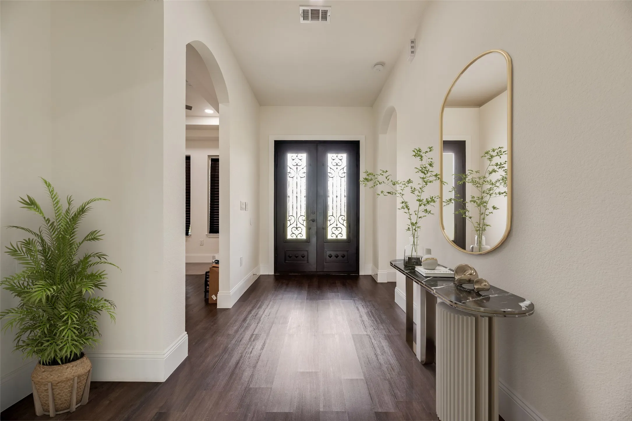 Arched doorways, dark wood-finish flooring, dark double entry doors with decorative glass and ironwork, and recessed lighting