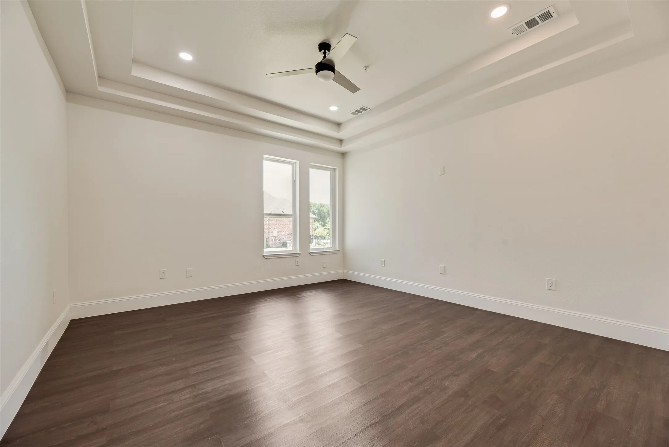 Tray ceiling with recessed lighting and a ceiling fan, complemented by wood-finish flooring and multiple windows