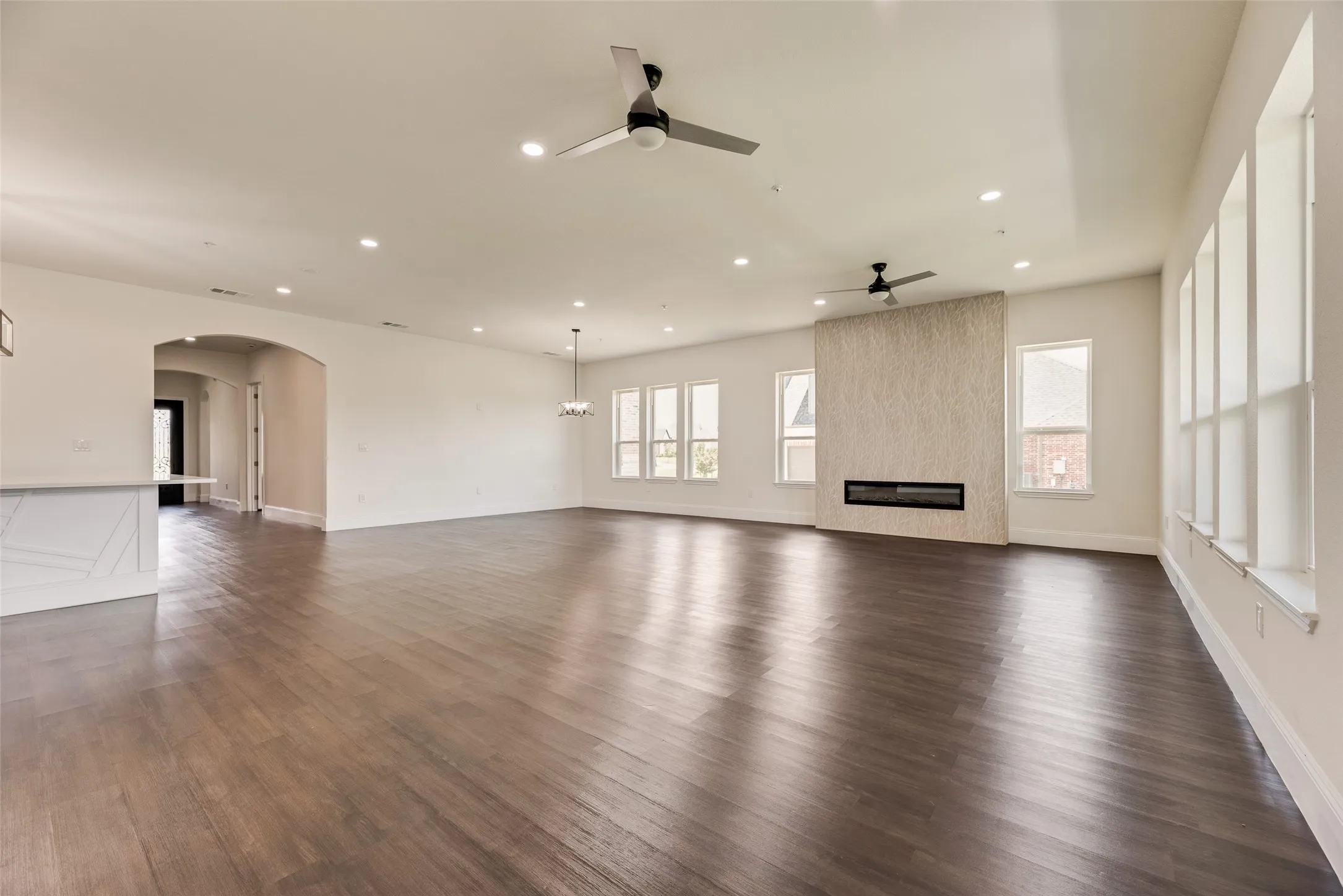 Expansive wood-finish flooring throughout, recessed lighting, and a linear fireplace with a textured surround