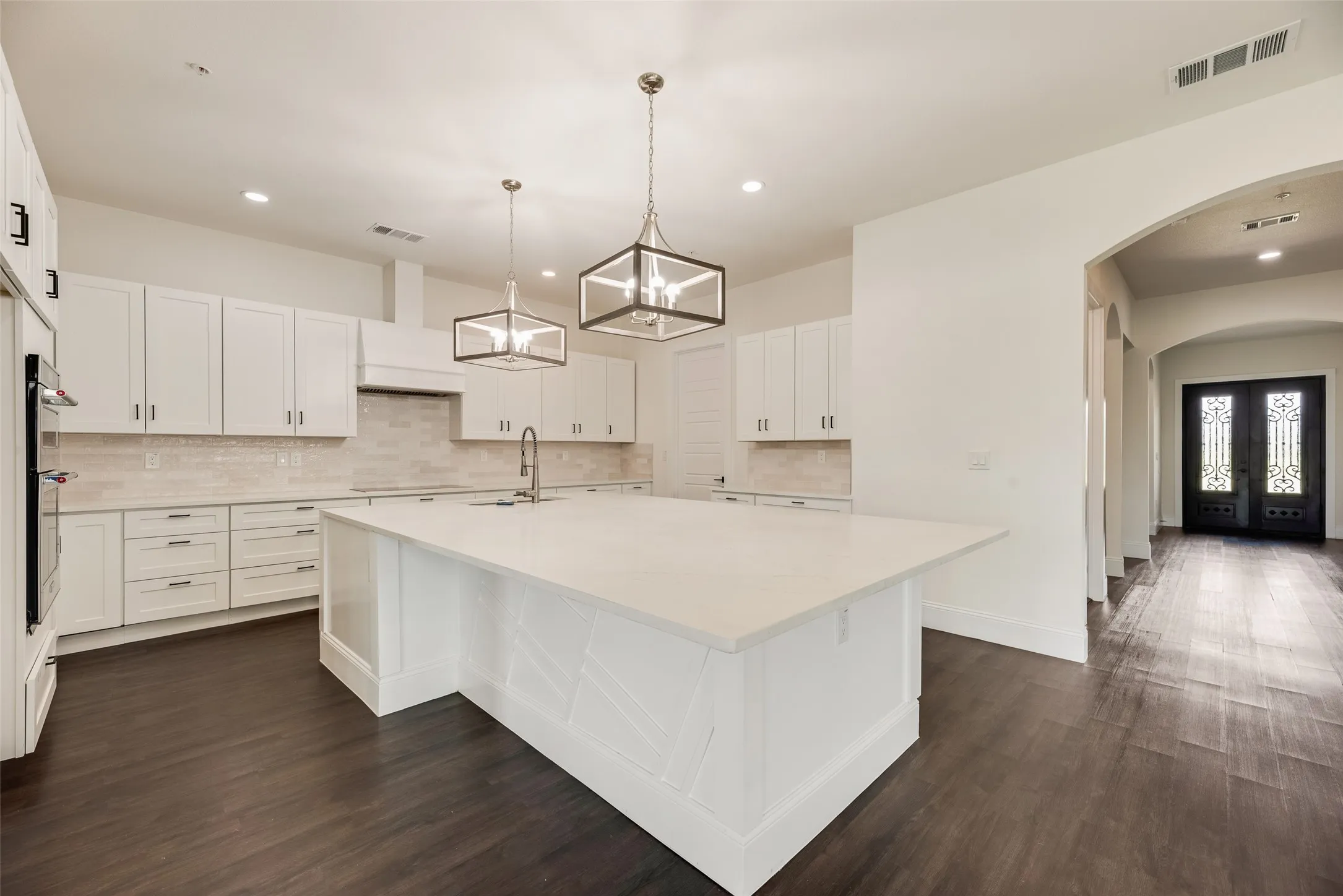 Kitchen featuring a large central island with a solid surface countertop, white shaker-style cabinetry, stainless steel built-in oven, and recessed lighting
