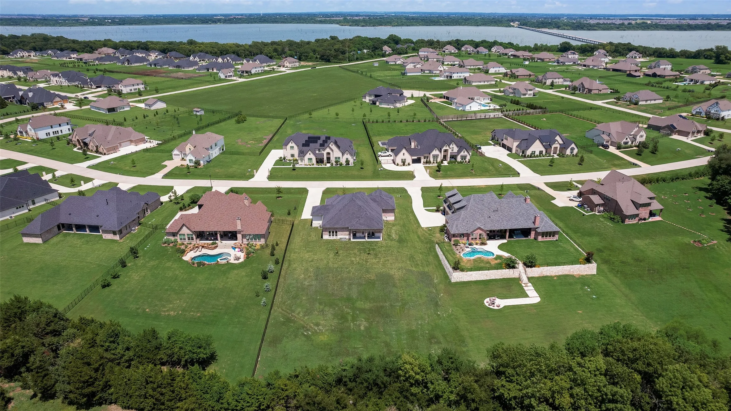 Expansive residential development featuring multiple properties, some with private pools, lush green landscaping, and paved driveways