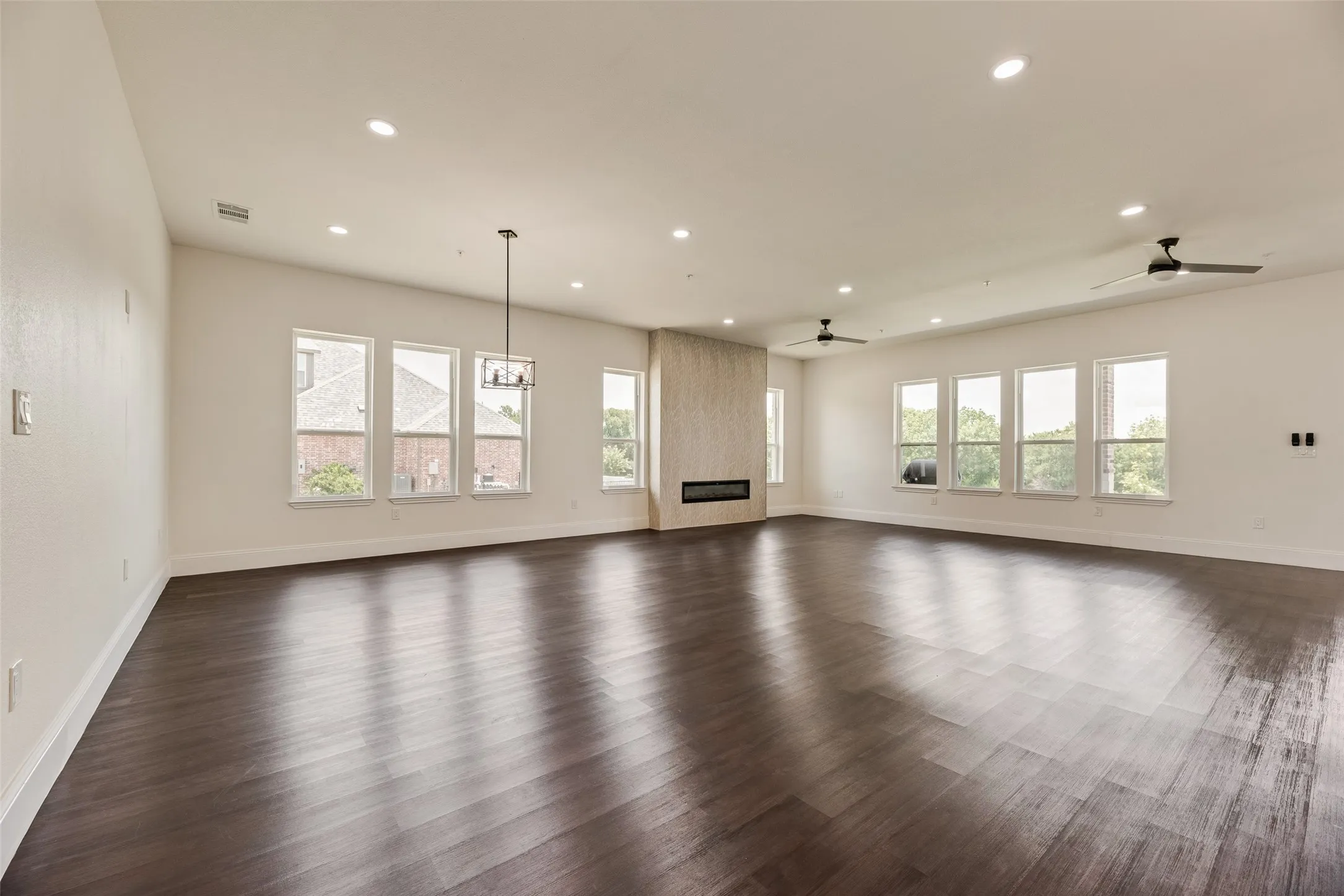 Spacious interior with dark wood-finish flooring, multiple recessed lighting fixtures, and a modern linear fireplace with a textured surround