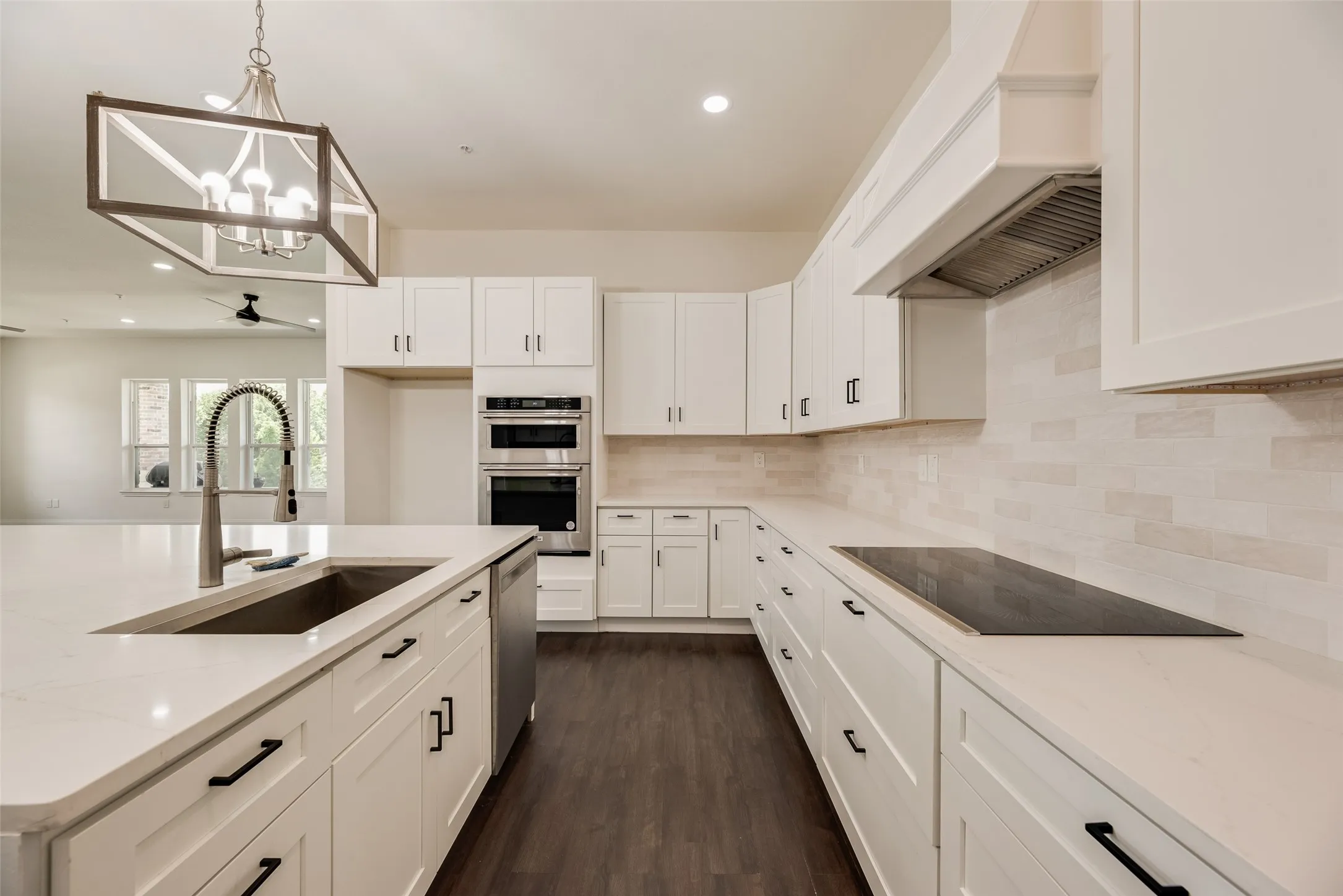 Kitchen featuring white cabinetry, light-toned countertops, integrated stainless steel appliances, dark wood-finish flooring, and a large center island with an undermount sink