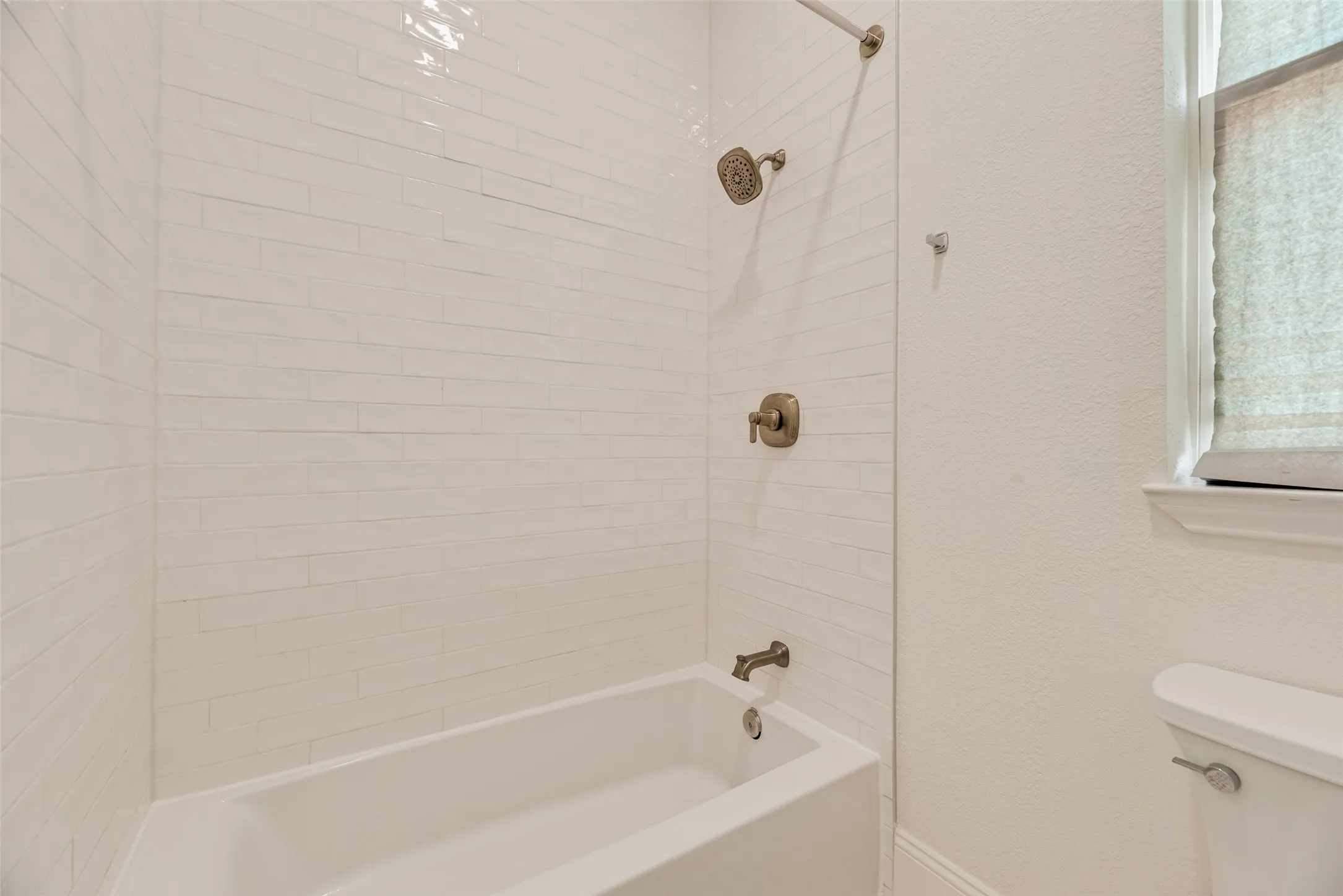 Tub and shower combination with white subway tile surround, bronze-finish fixtures, and clear glass shower panel