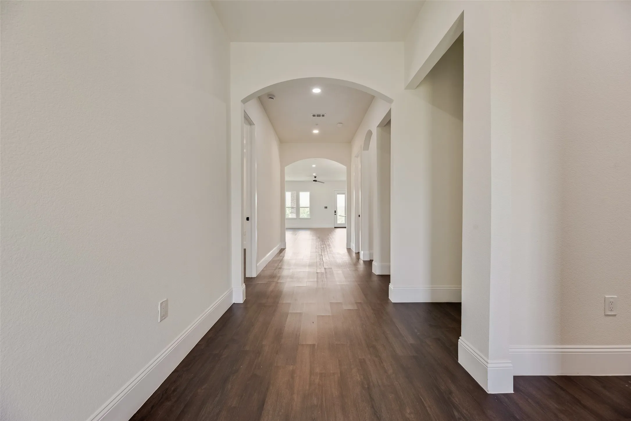 Hallway with dark wood-finish flooring, recessed lighting, and arched doorways
