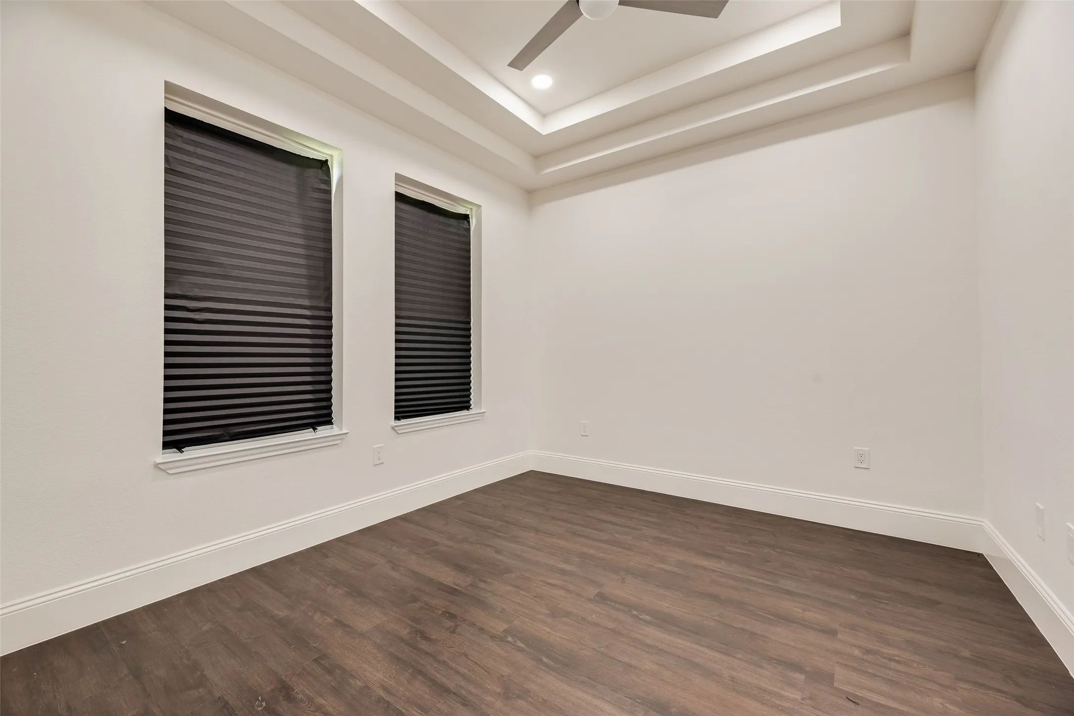 Tray ceiling with recessed lighting and a ceiling fan, wood-finish flooring, and two windows with blinds