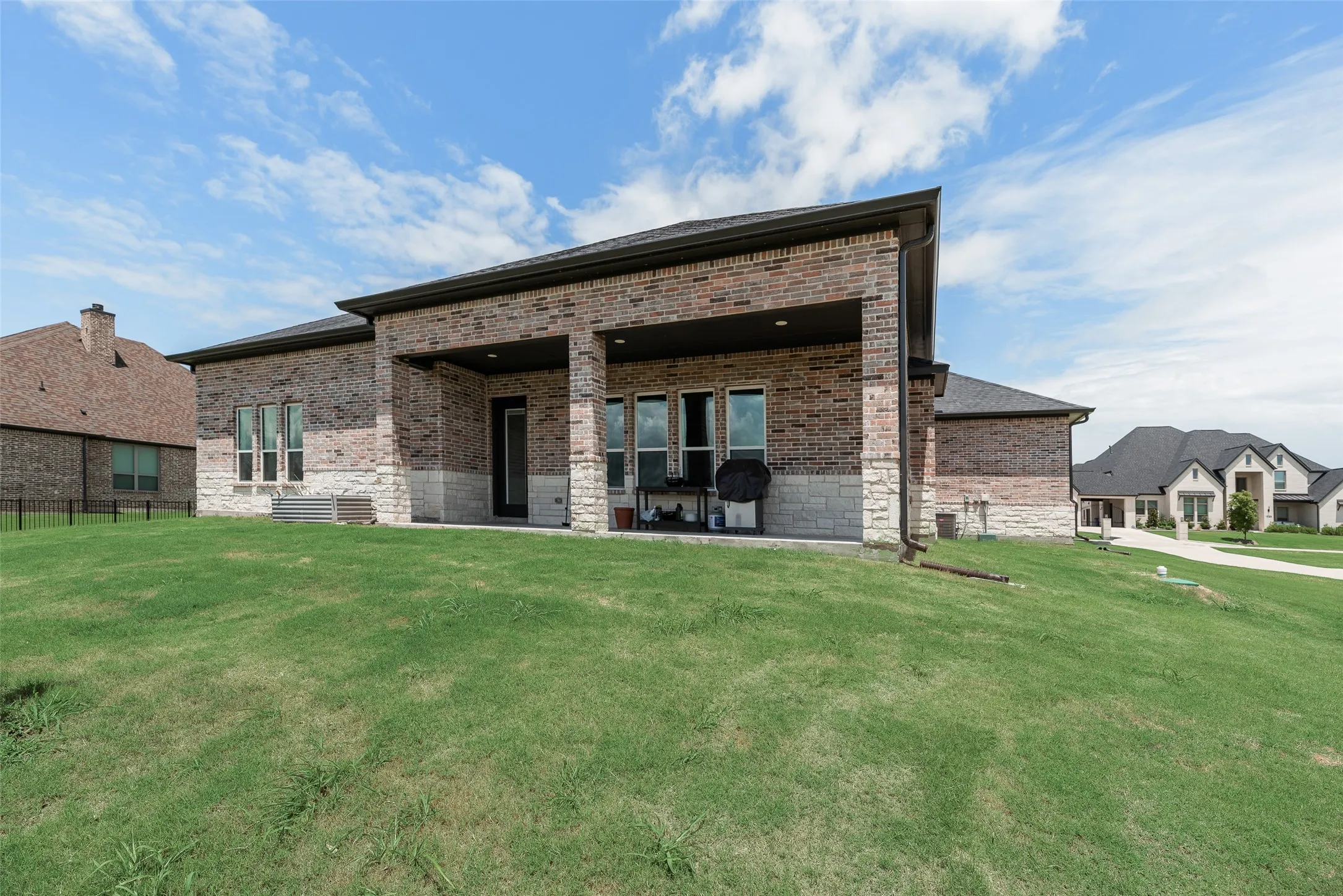 Brick exterior with stone accents, covered patio, multiple windows, and a sloped lawn