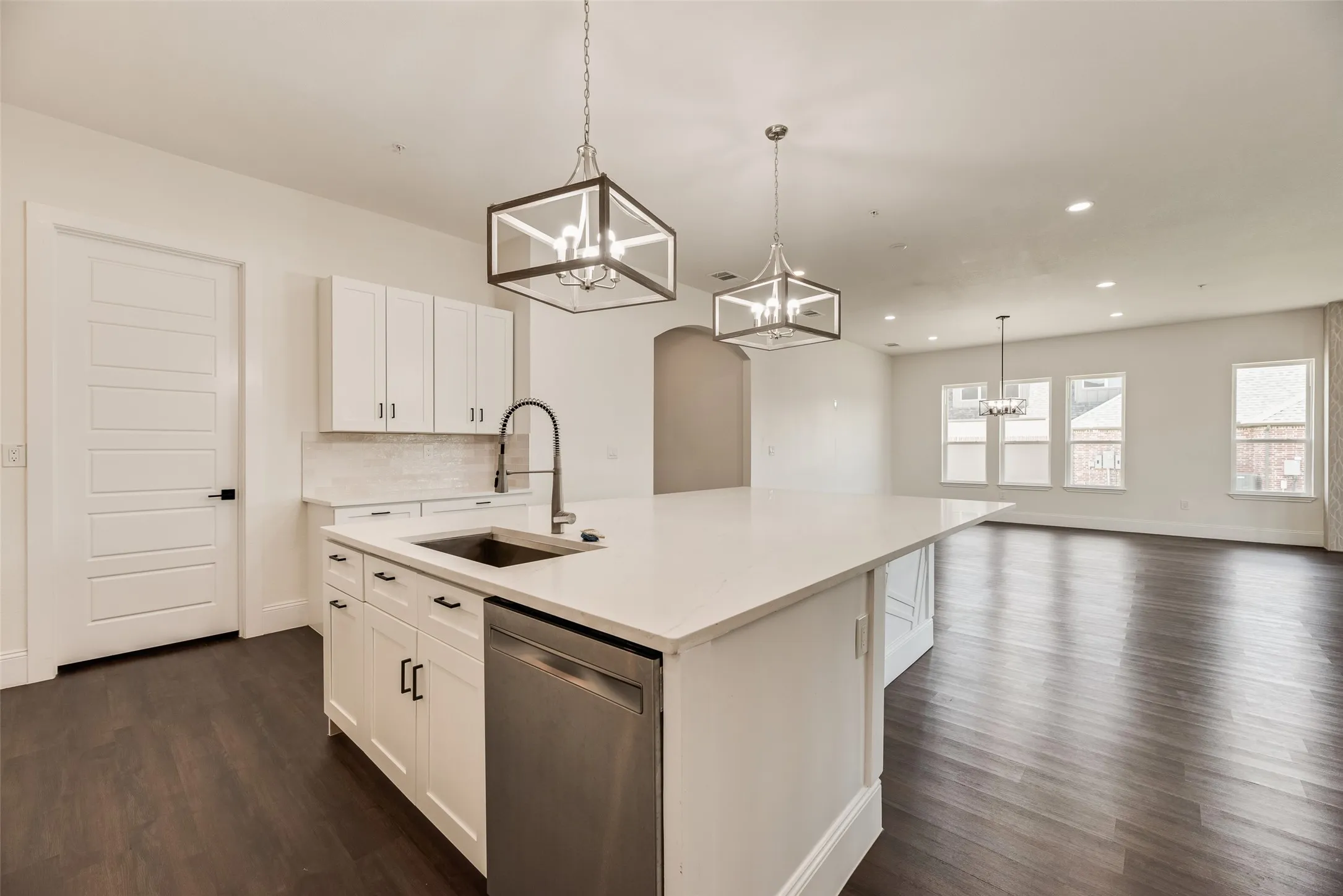 Spacious open-concept interior featuring wood-finish flooring, a large kitchen island with a sink, white cabinetry, and stainless steel appliances