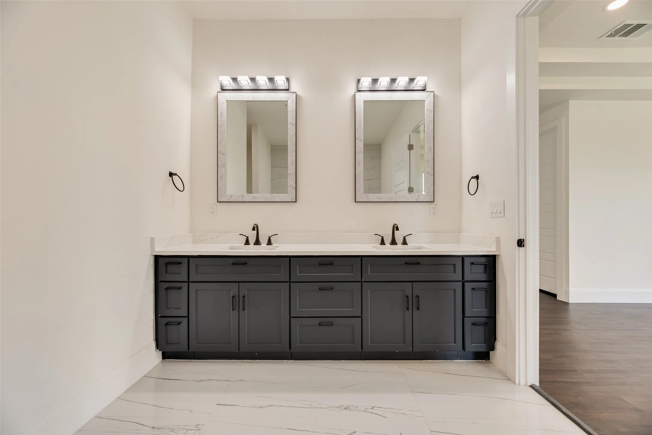 Dual vanity with dark cabinetry, white countertops, two framed mirrors, and black fixtures