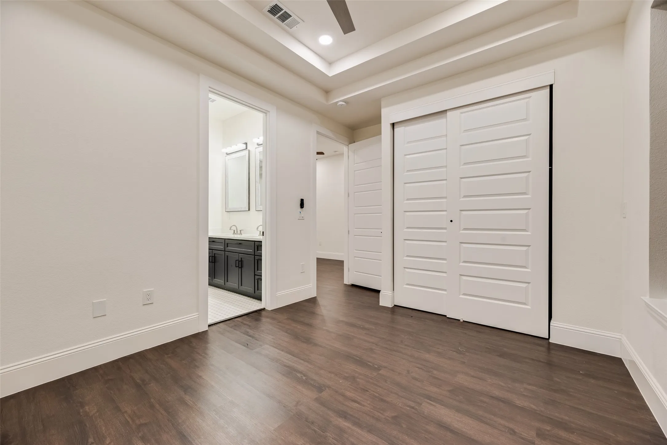 Wood-finish flooring, recessed ceiling with accent lighting, white trim and baseboards, and sliding panel closet doors