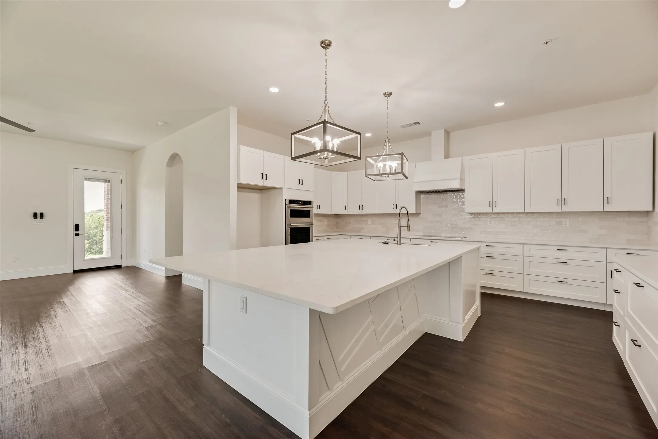 Spacious kitchen featuring an expansive central island with a light-toned countertop, white cabinetry with dark hardware, a tile backsplash, and wood-finish flooring