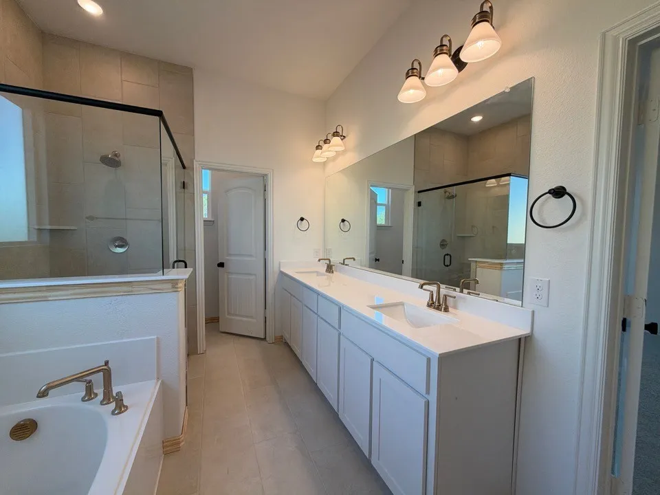 Dual sink vanity with white cabinetry and light-toned countertops, featuring a separate shower with glass enclosure and a built-in bathtub with a gold-tone faucet