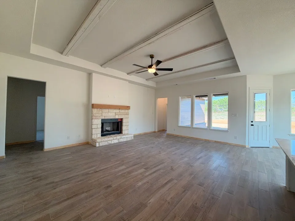 Spacious living area featuring a stone-clad fireplace with a wood mantel, wood-finish flooring, and a tray ceiling with exposed beams