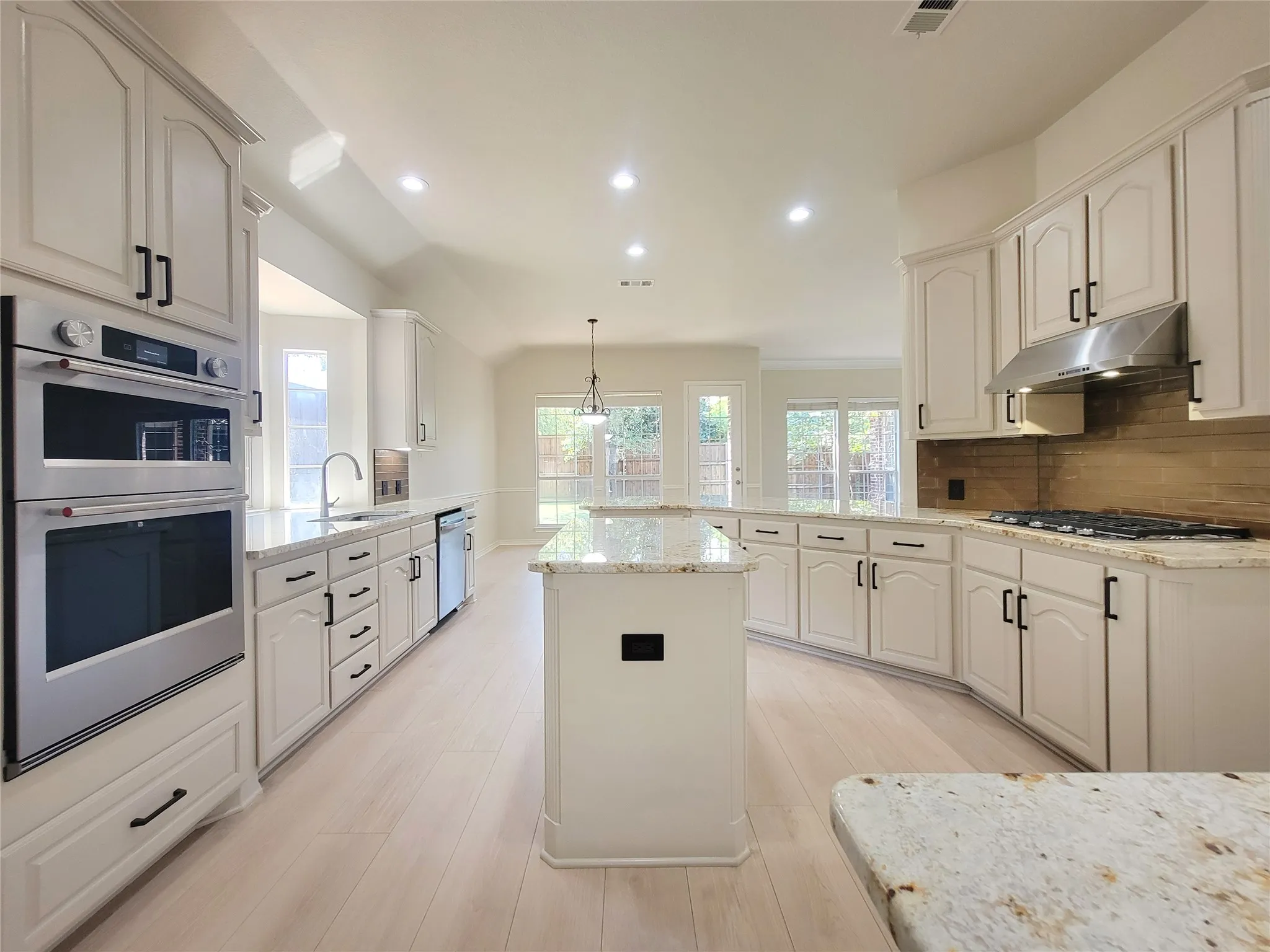 Kitchen featuring white cabinetry, stainless steel appliances, granite countertops, wood-finish flooring, and a tiled backsplash