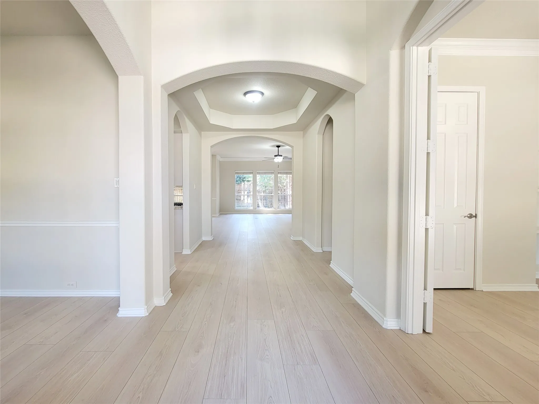 Arched doorways, tray ceilings with recessed lighting, wood-finish flooring, and white trim