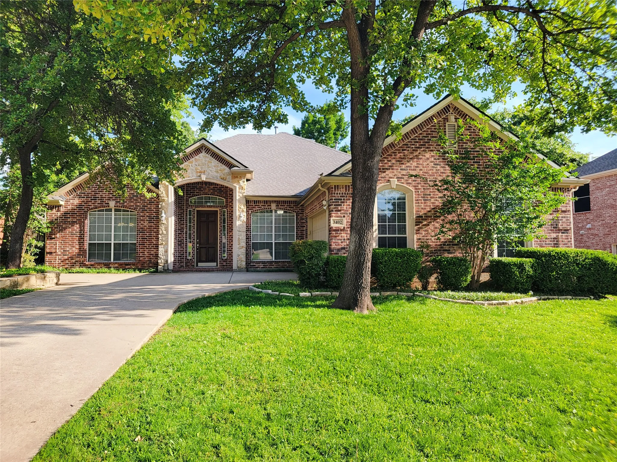 Brick and stone facade with arched entry, gabled roofline, and mature landscaping