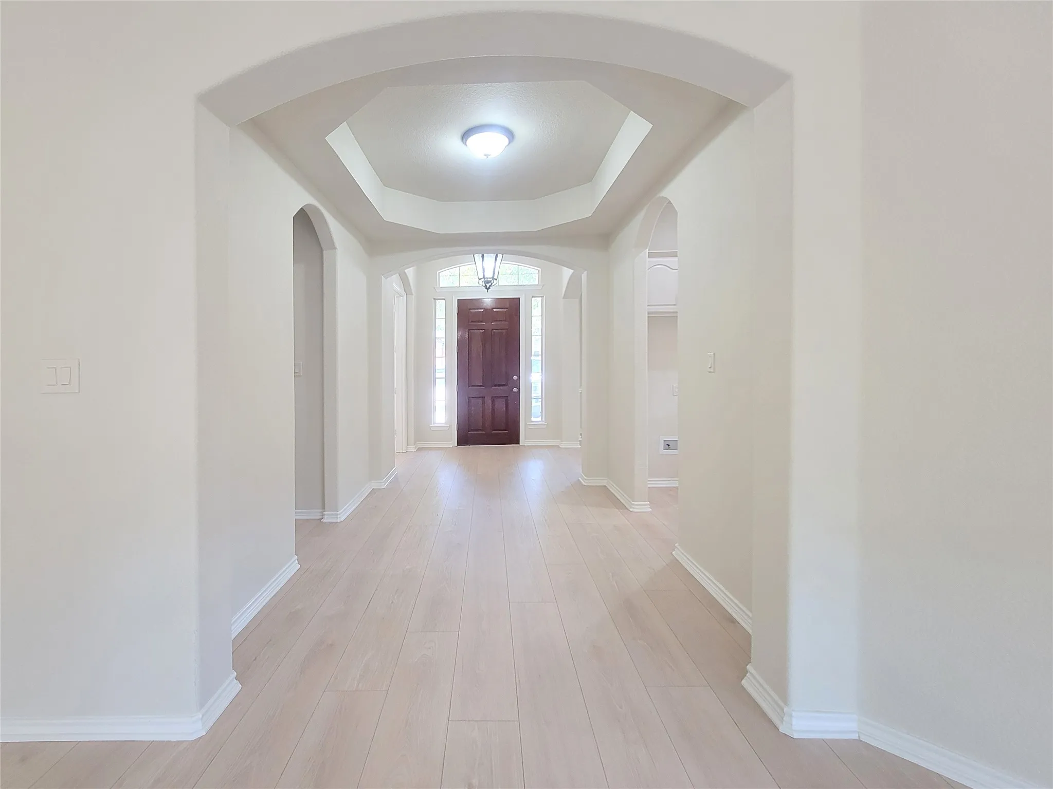 Wood-finish flooring throughout, featuring arched doorways and a tray ceiling with recessed lighting