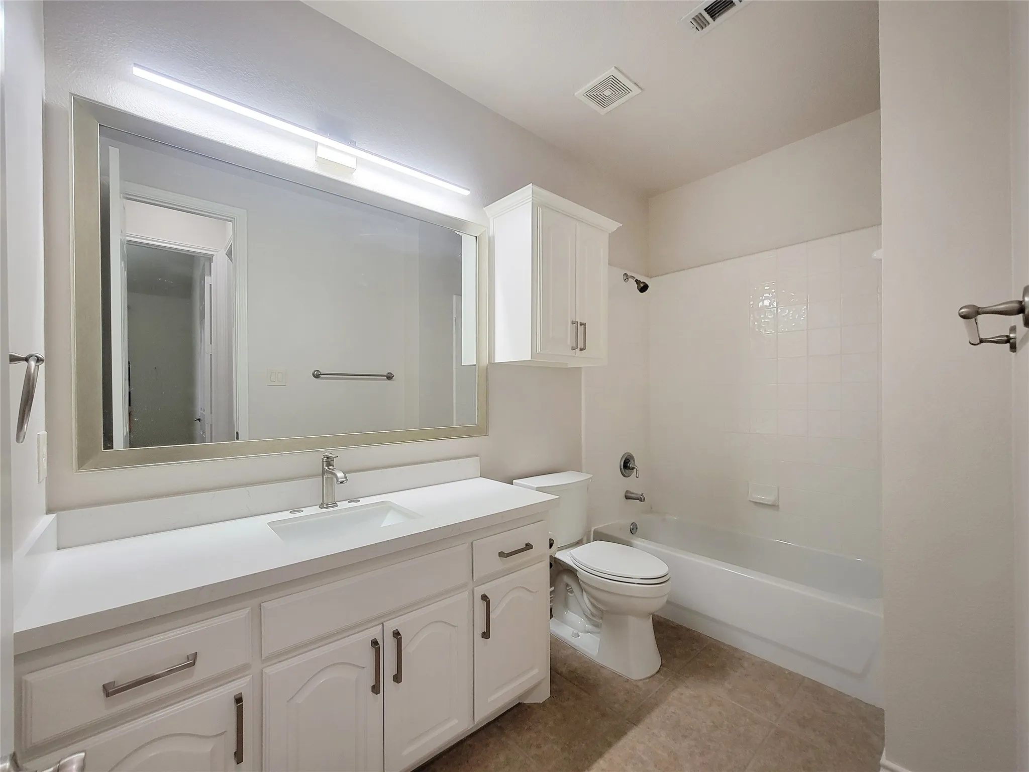Vanity with integrated sink and white countertop, white cabinetry with brushed nickel hardware, framed mirror, and a white tub with tile surround
