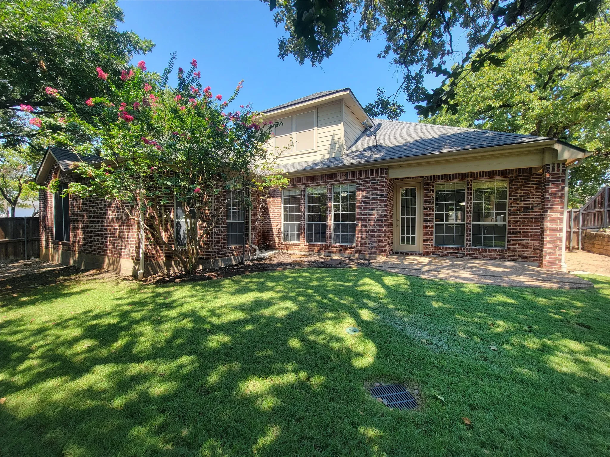 Brick exterior with multiple large windows, covered patio, and mature landscaping