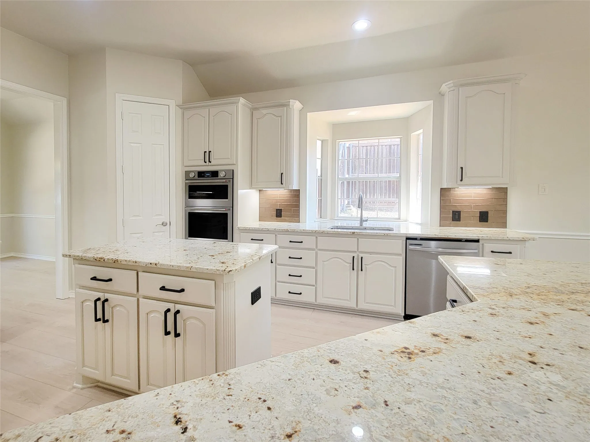 White kitchen cabinetry with black hardware, stone countertops, stainless steel appliances, and wood-finish flooring
