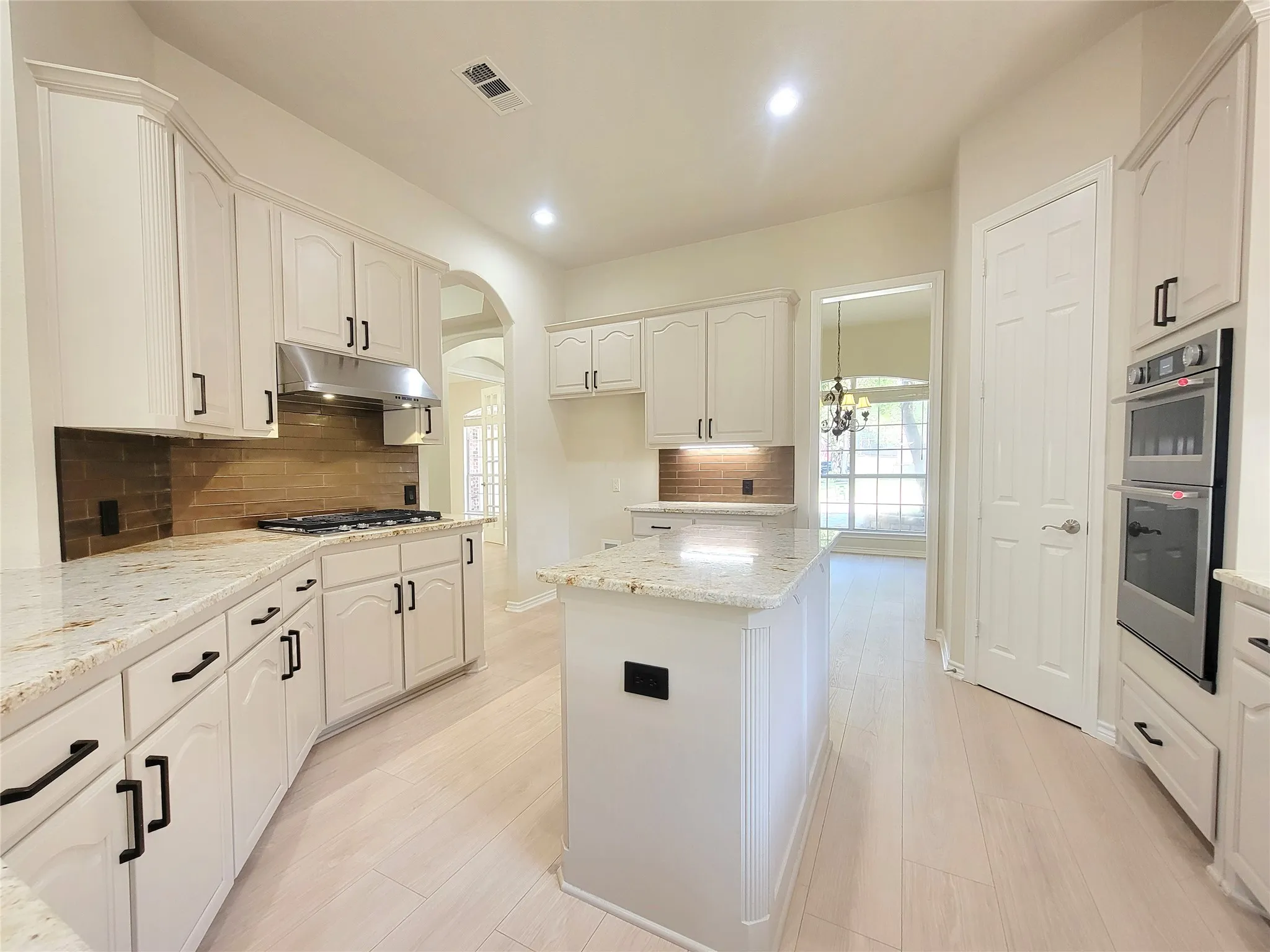 White cabinetry with black hardware, light-toned wood-finish flooring, granite countertops, stainless steel appliances, and a central island