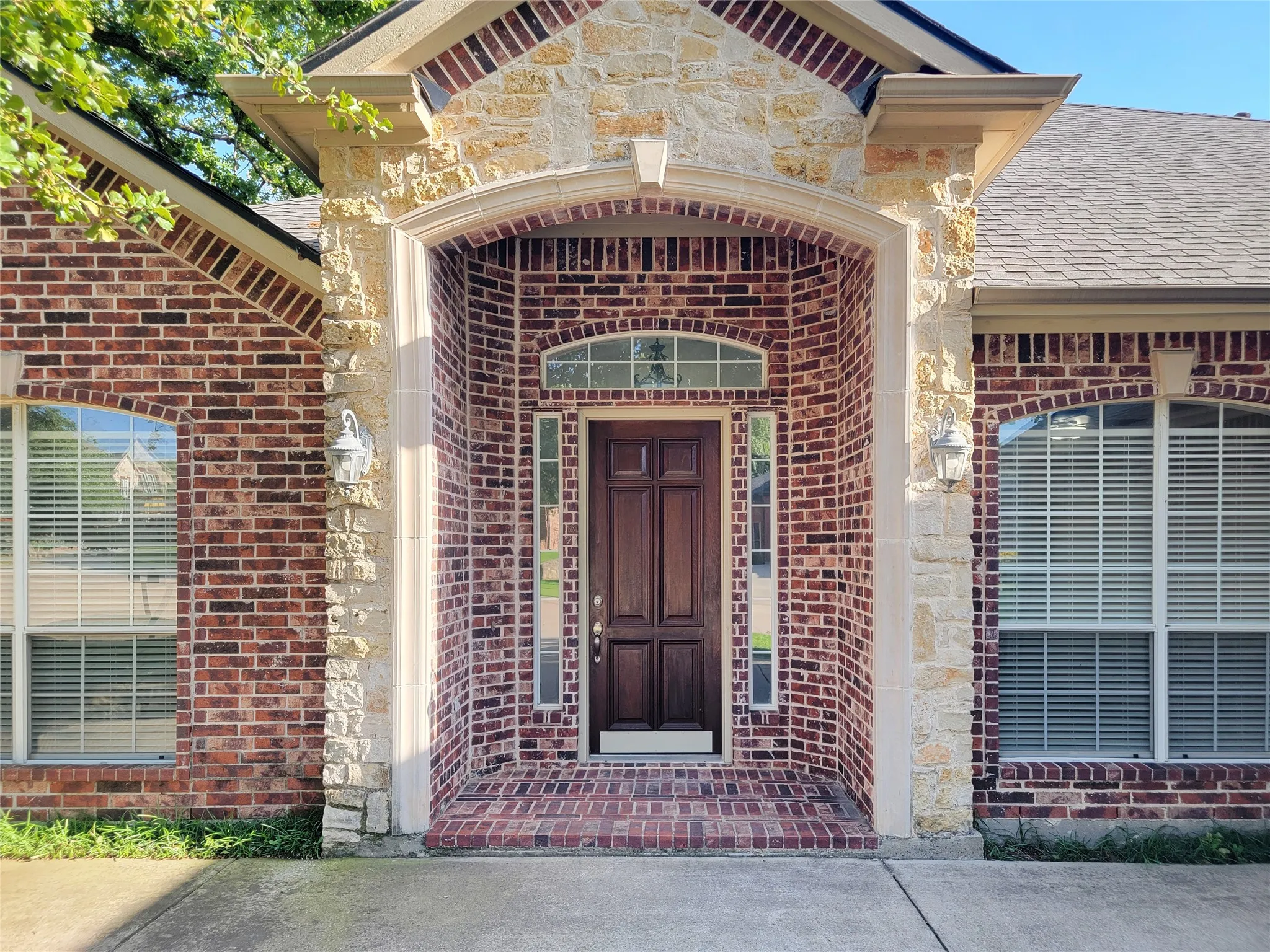 Brick and stone exterior featuring an arched entry, a paneled wood door with sidelights, and exterior sconce lighting