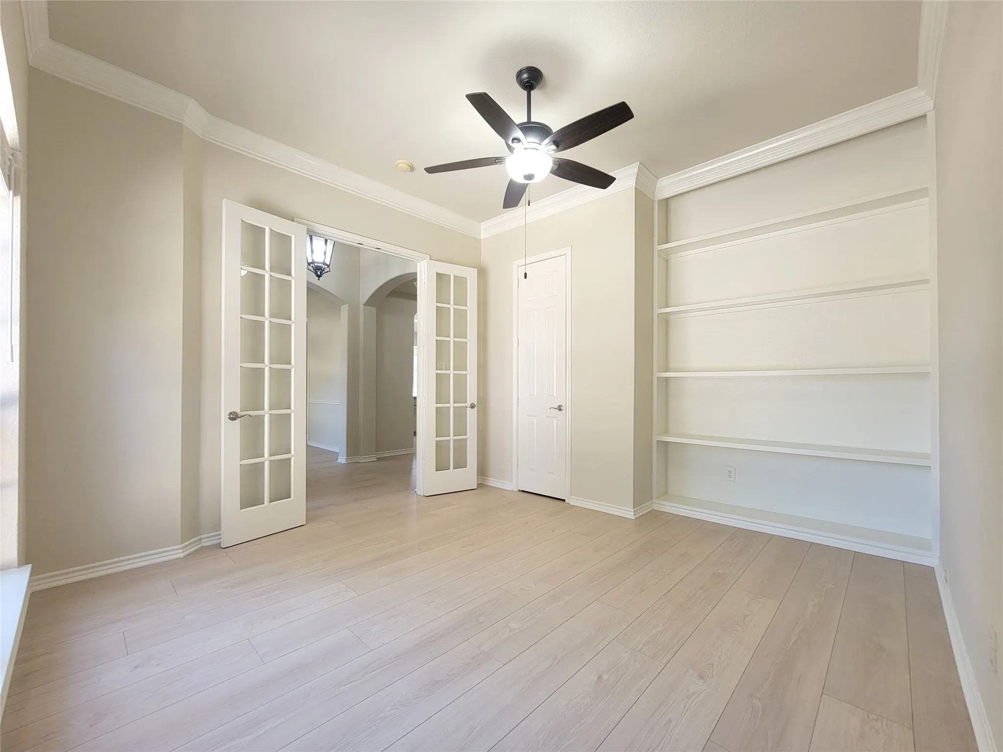 Wood-finish flooring, built-in shelving, French doors, crown molding, and a ceiling fan