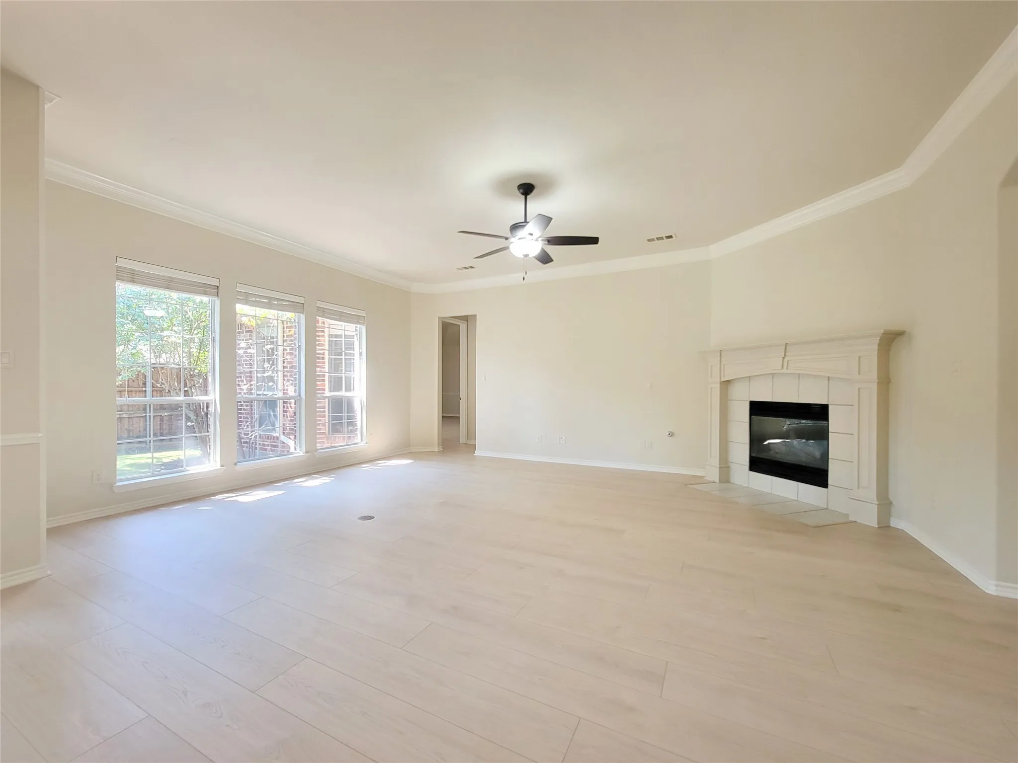 Spacious room featuring light wood-finish flooring, a ceiling fan, and crown molding