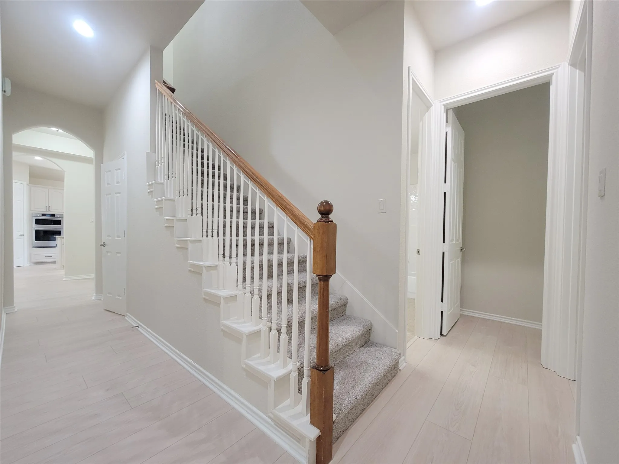 Wood-finish flooring, staircase with wood handrail, carpeted stairs, and arched doorway