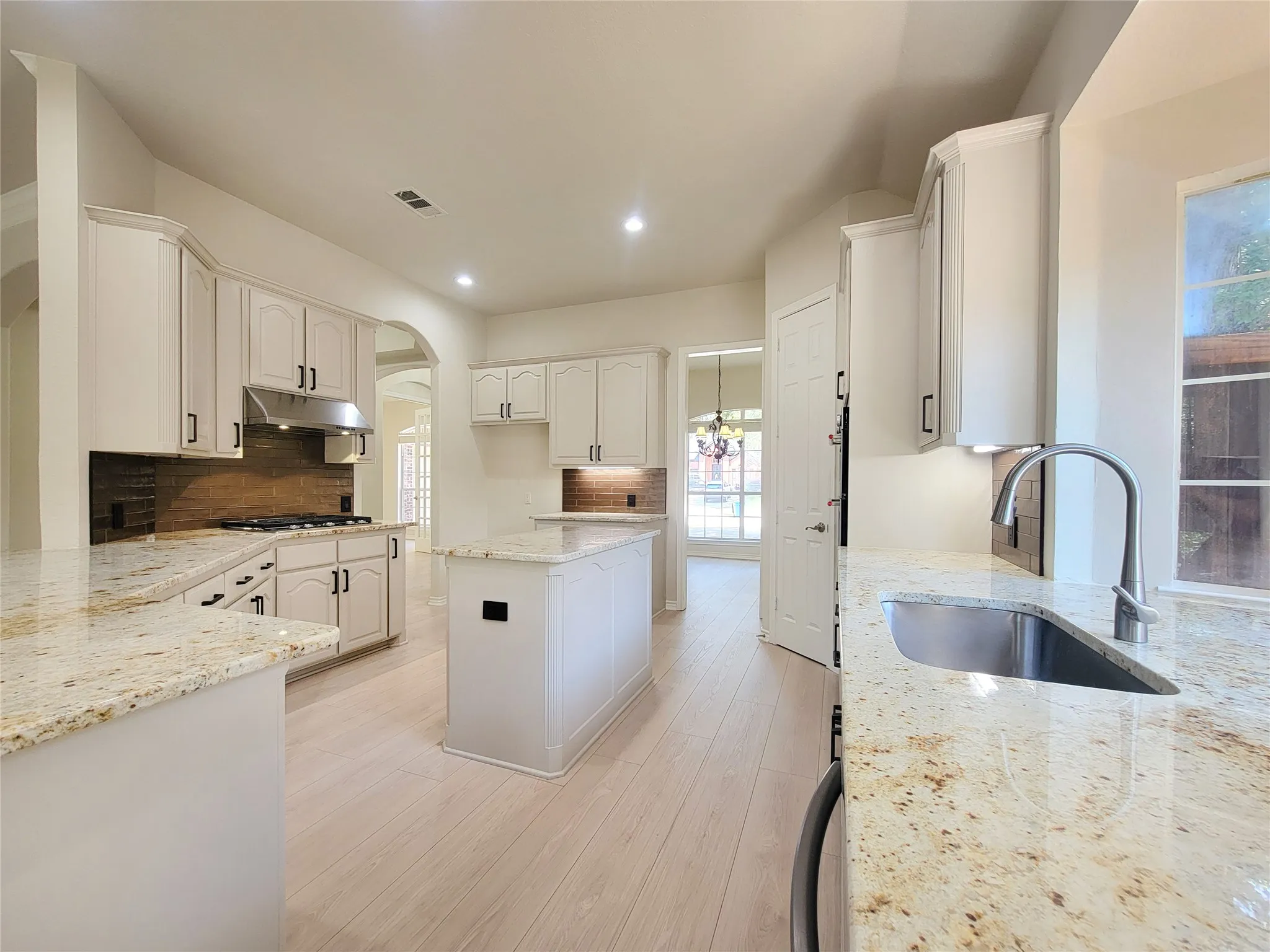 Kitchen featuring light wood-finish flooring, white cabinetry with black hardware, stone countertops, a center island, and an undermount stainless steel sink