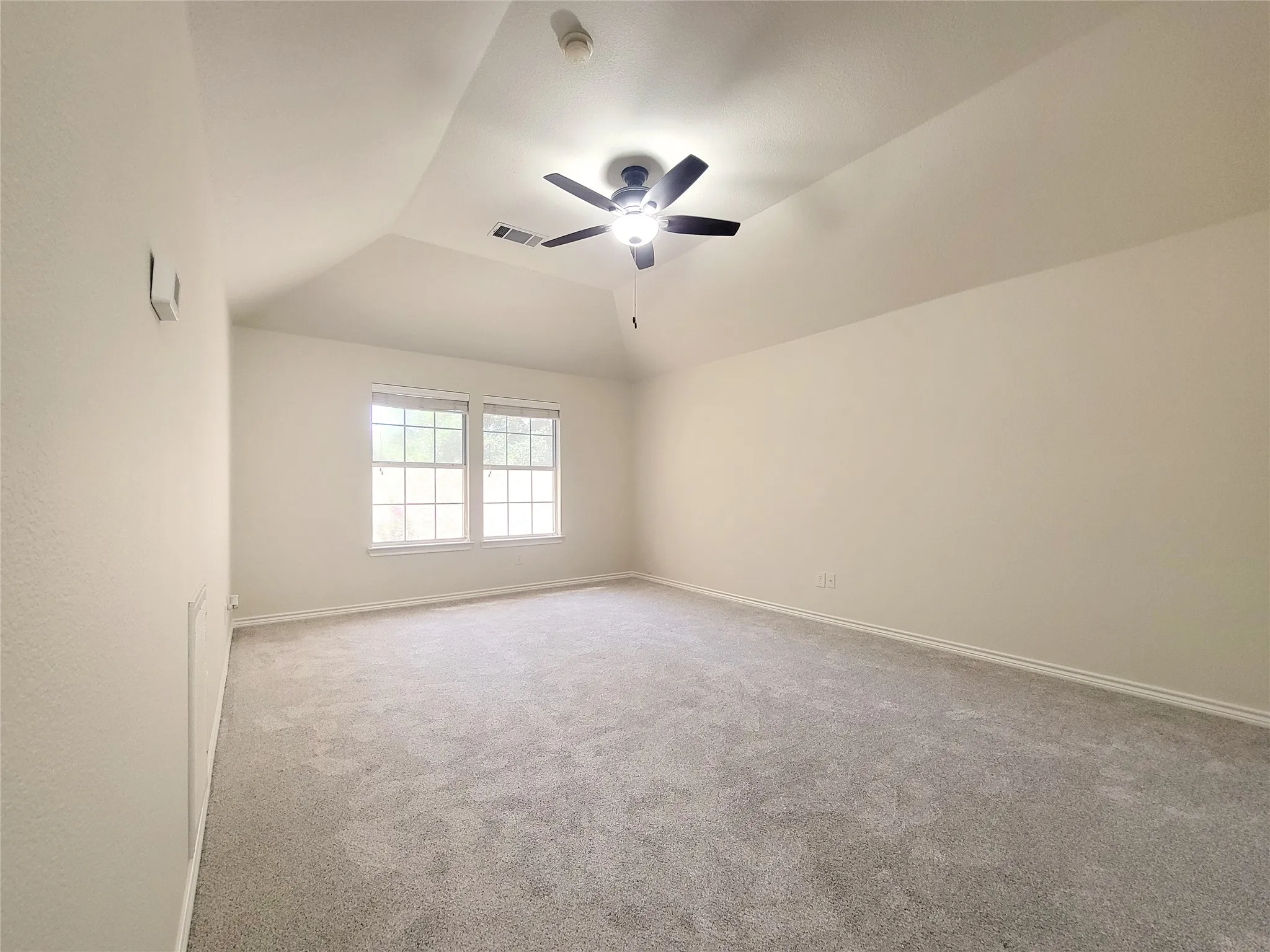 Vaulted ceiling with an installed ceiling fan, dual windows, and light gray carpeting