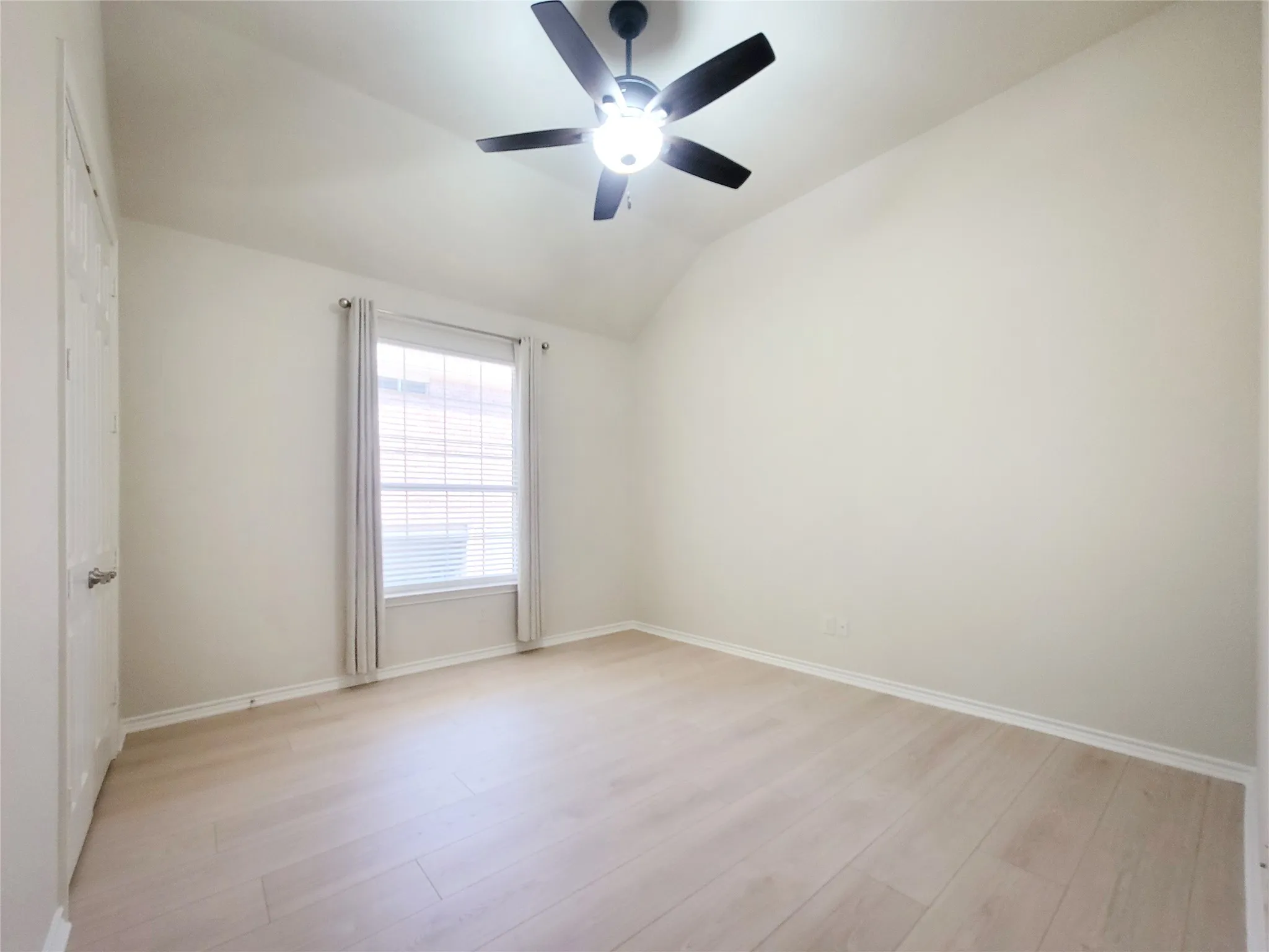 Vaulted ceiling with a ceiling fan, light wood-finish flooring, and window with blinds