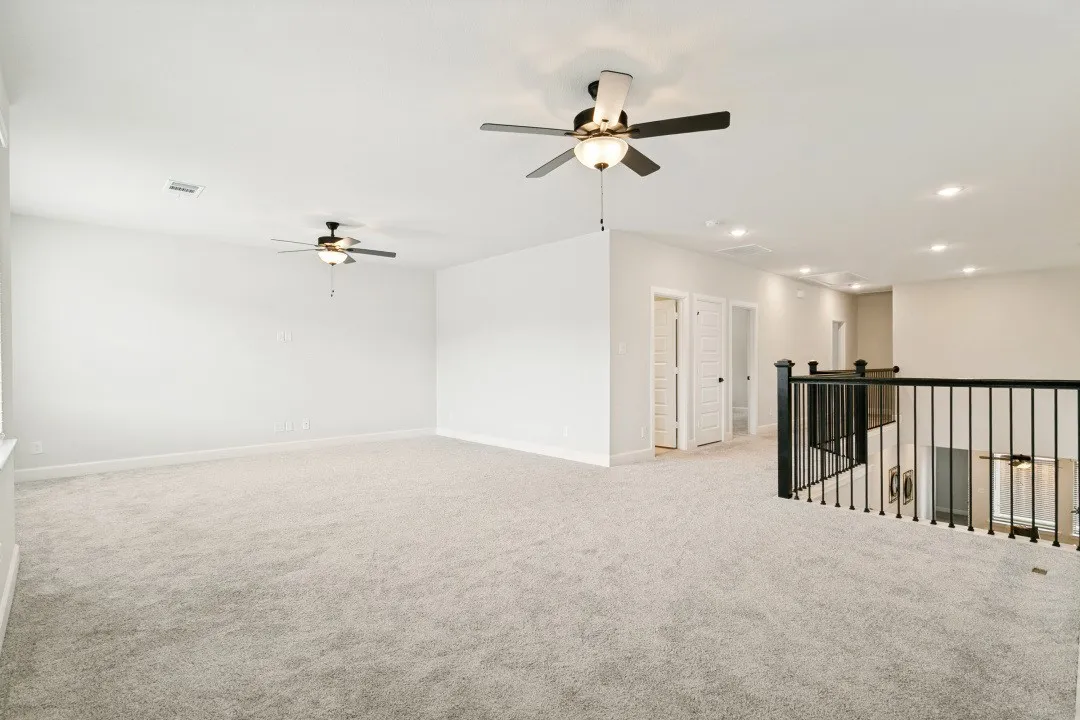 Expansive carpeted loft space featuring multiple ceiling fans with integrated lighting, recessed lighting, and a black wrought iron baluster railing