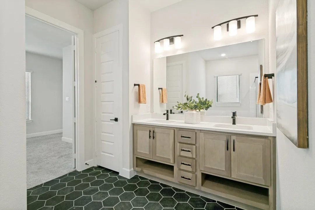 Dual vanity with integrated sinks, light-toned cabinetry, and black hexagonal floor tiling