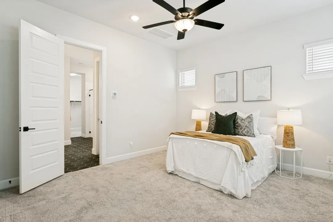Carpeted bedroom featuring white walls, a ceiling fan with integrated lighting, and two windows with horizontal blinds