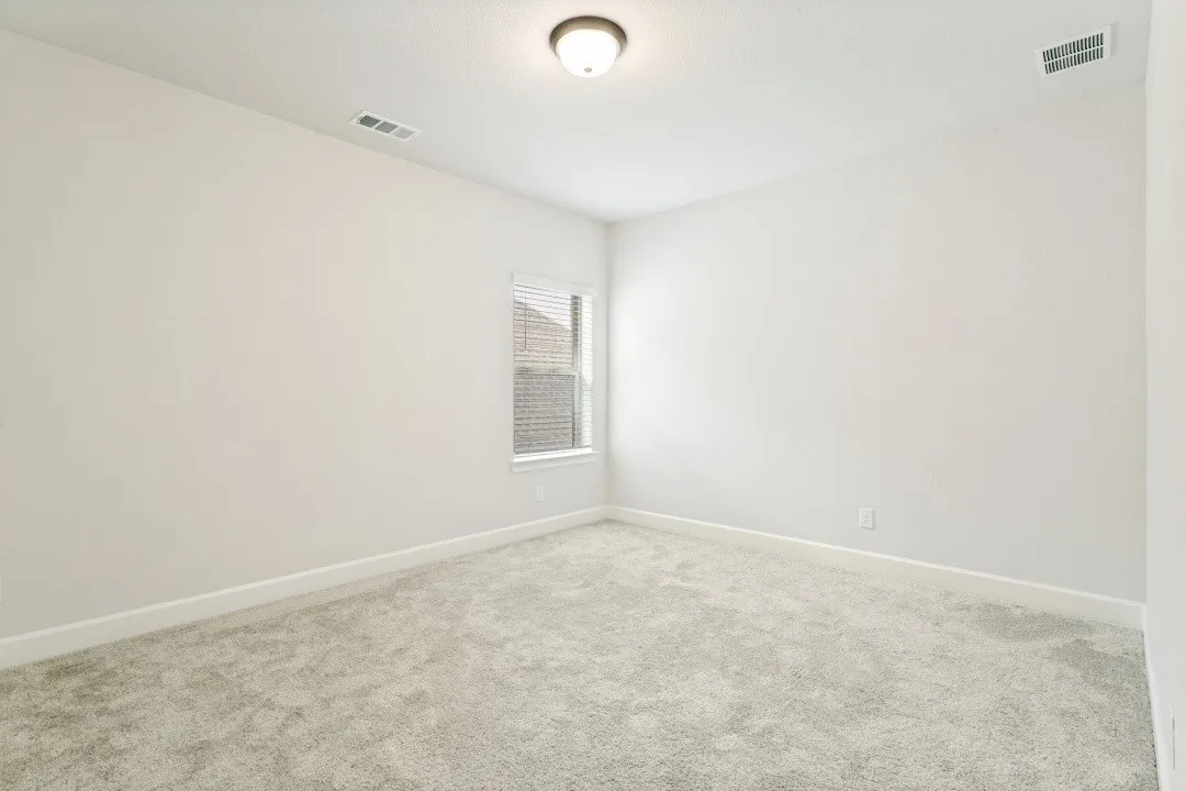 Bright interior space featuring light-colored carpeting, white baseboards, and a window with blinds
