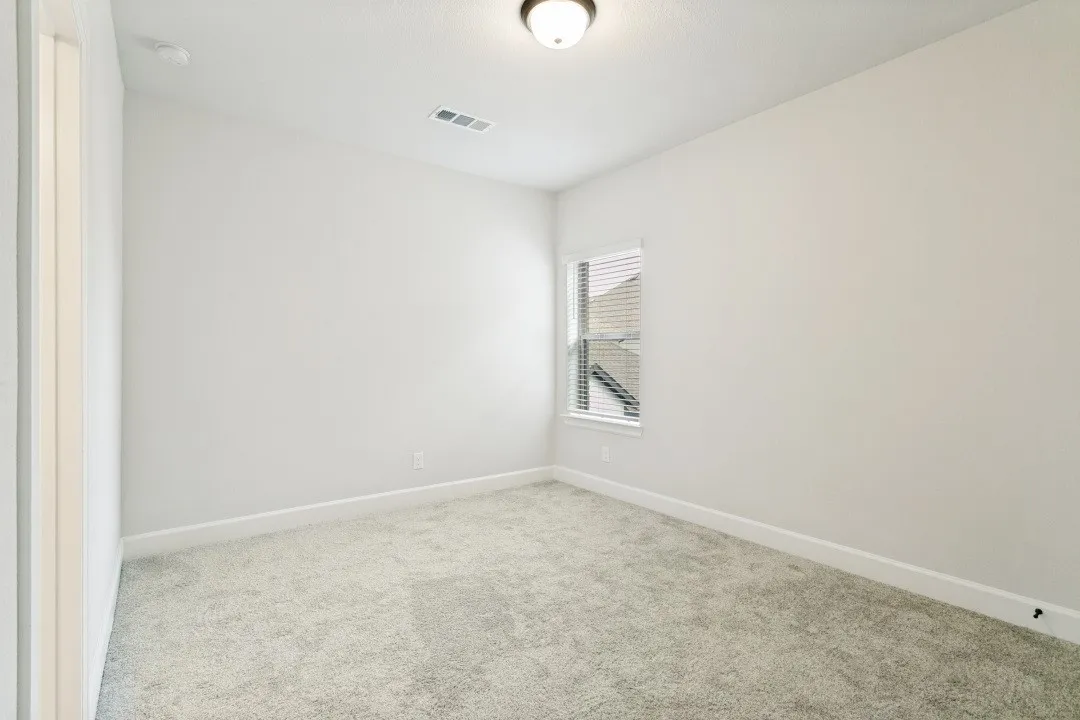 Bright room featuring plush gray carpeting, white baseboards, a single window with blinds, and a flush-mount ceiling light fixture