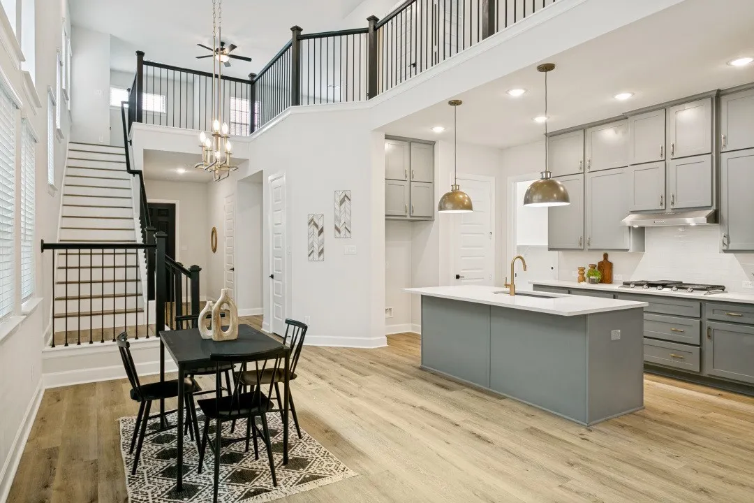 Open-concept living area featuring a kitchen with gray cabinetry and white countertops, a central island with a sink and pendant lighting, and light wood-finish flooring