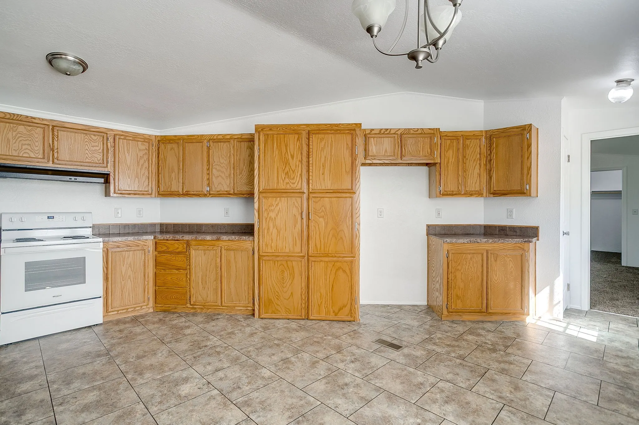 Spacious kitchen featuring abundant wood-finish cabinetry, tile flooring, and white appliances including a built-in electric range