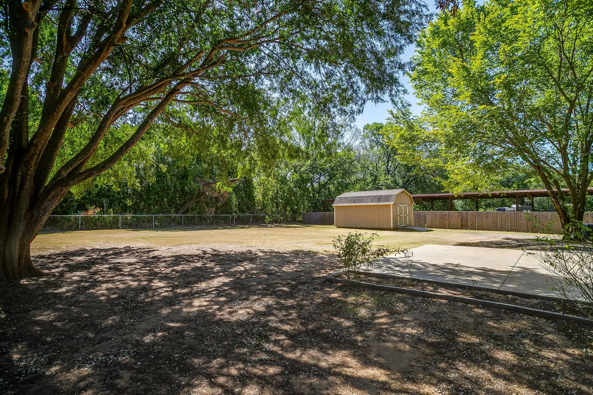 Expansive grounds featuring mature shade trees, open lawn space, and a detached wood-finish outbuilding with metal roofing