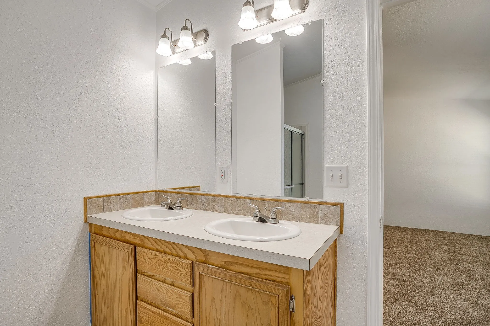 Double-sink vanity with wood cabinetry, white countertop, and dual chrome faucets